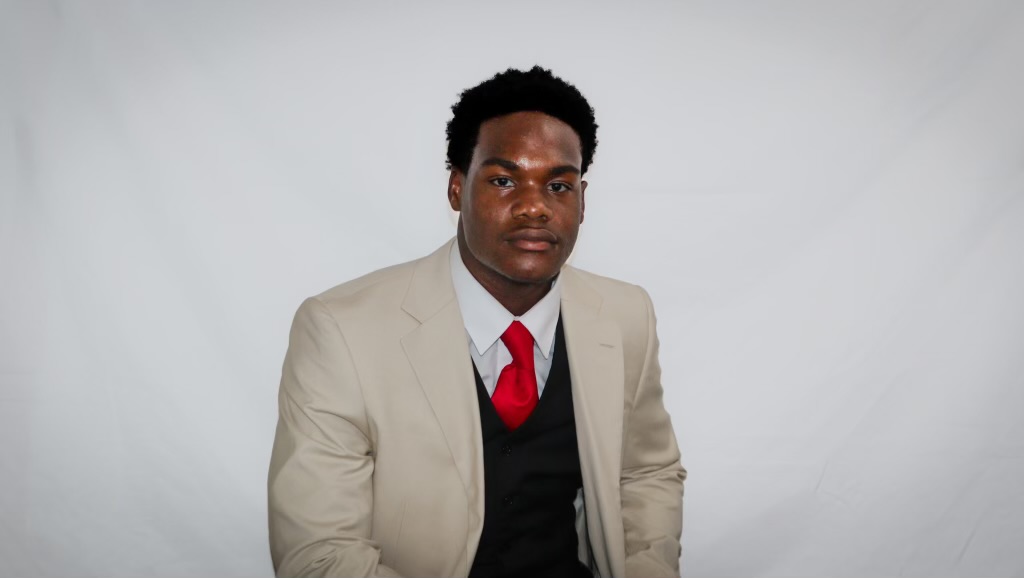 AJ standing in a tan suit and red tie